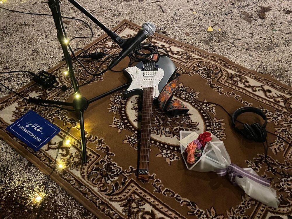 A guitar resting on a patterned carpet surrounded by string lights