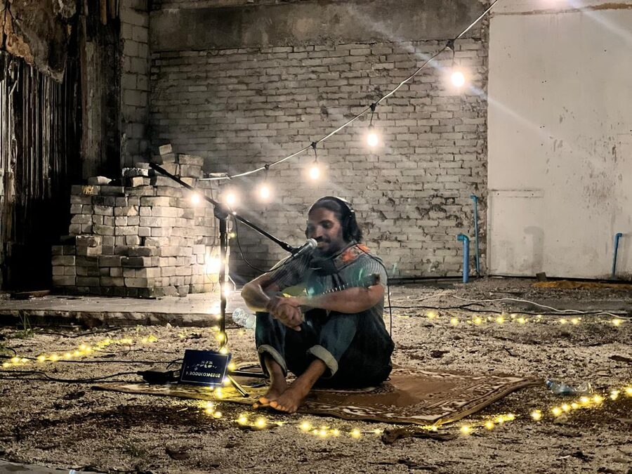 Cross-legged in a bare brick room ringed by string lights