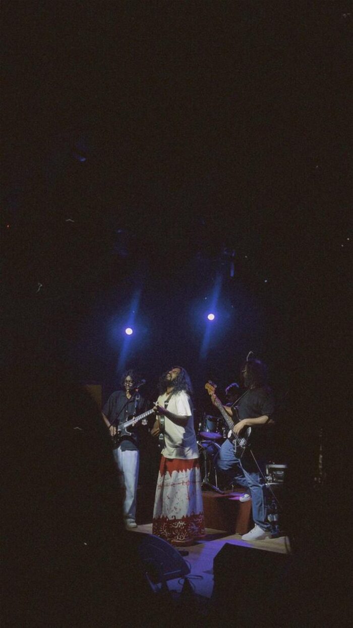 The band on a dark stage under two blue beams of light
