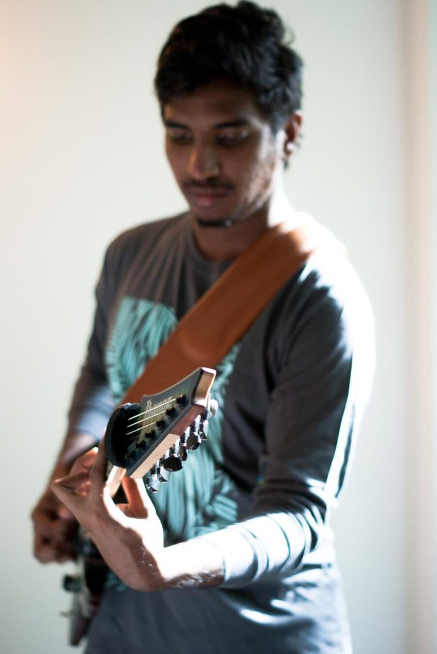 Flanbeha playing guitar by a window, head bowed
